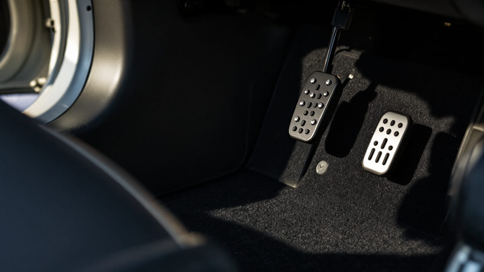 Driver's footwell of a performance car showing the accelerator pedal and floor mat in soft daylight